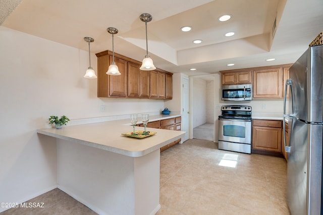 kitchen with a tray ceiling, light countertops, appliances with stainless steel finishes, brown cabinetry, and a peninsula