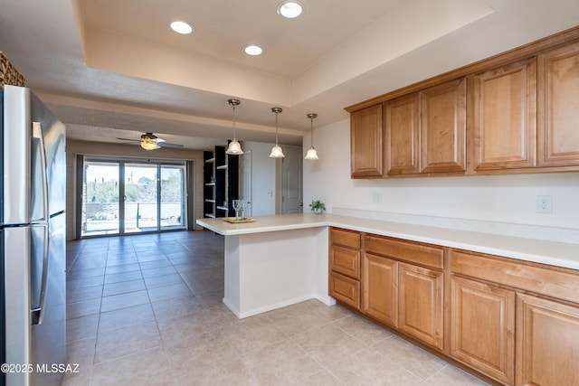 kitchen with a tray ceiling, light countertops, freestanding refrigerator, open floor plan, and a peninsula