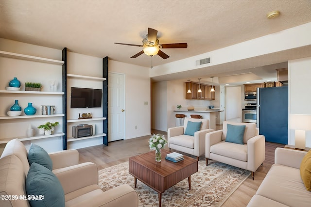 living room featuring a ceiling fan, light wood-type flooring, visible vents, and a textured ceiling