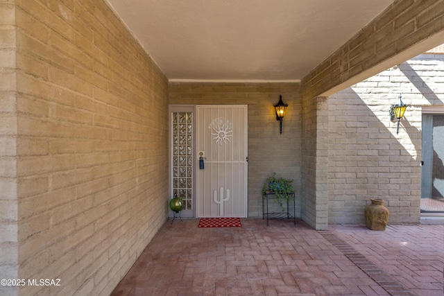 view of exterior entry with brick siding and a patio