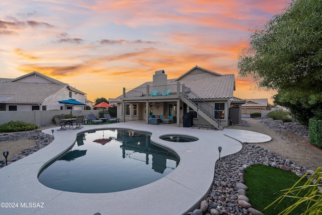 pool at dusk with an in ground hot tub, a patio, and an outdoor hangout area