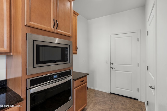 kitchen with appliances with stainless steel finishes, dark stone counters, and light tile patterned flooring