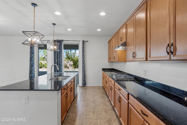 kitchen with sink, stainless steel appliances, dark stone counters, pendant lighting, and a kitchen island with sink