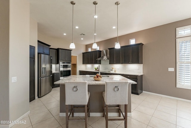 kitchen with a center island, stainless steel appliances, wall chimney range hood, light stone counters, and pendant lighting