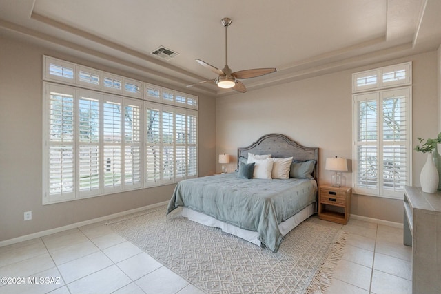 tiled bedroom with a tray ceiling, multiple windows, and ceiling fan