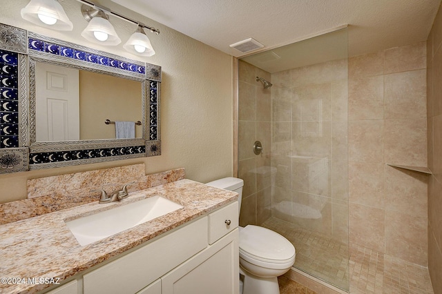 bathroom with vanity, toilet, a textured ceiling, and a tile shower