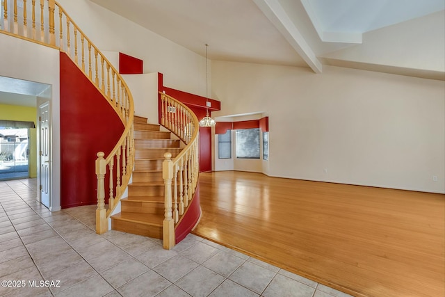 stairway with tile patterned floors, a towering ceiling, beam ceiling, and a notable chandelier