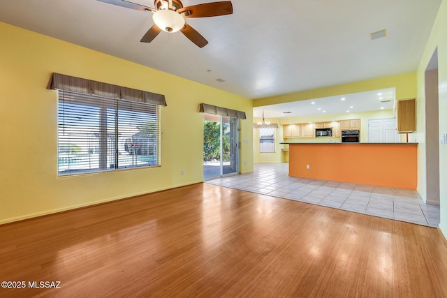 unfurnished living room featuring ceiling fan with notable chandelier and light hardwood / wood-style flooring