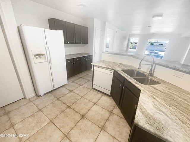 kitchen featuring light stone counters, white appliances, dark brown cabinetry, sink, and light tile patterned flooring