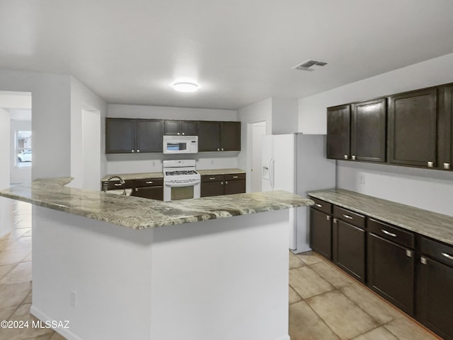 kitchen featuring light tile patterned flooring, dark brown cabinetry, white appliances, and a kitchen island with sink