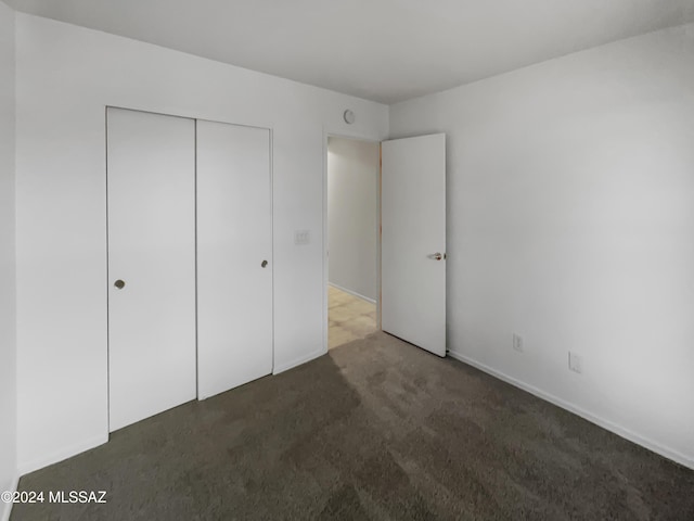 unfurnished bedroom with dark carpet and a closet