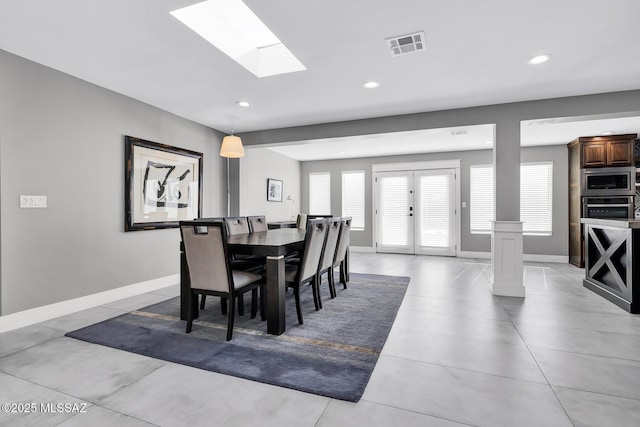 dining room with ornate columns, a skylight, and french doors