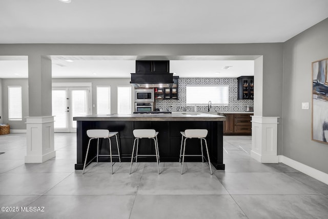 kitchen with stainless steel appliances, a kitchen island, a kitchen bar, and decorative columns