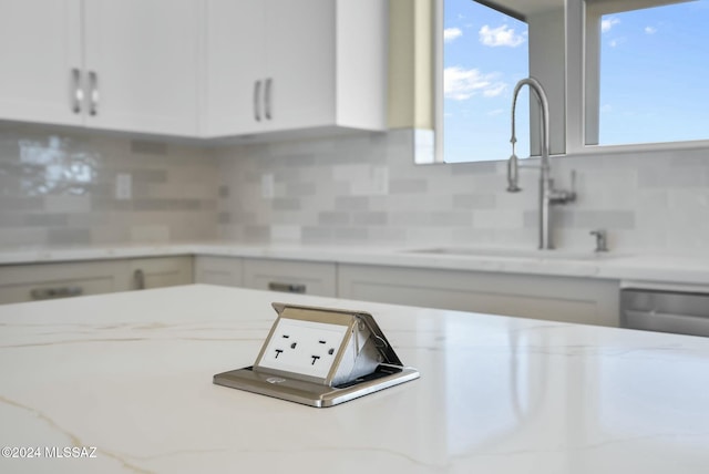 kitchen with light stone countertops, backsplash, white cabinetry, and sink