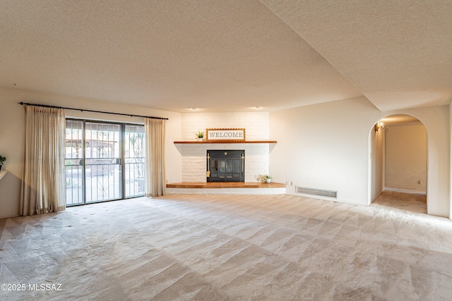 unfurnished living room with light carpet, a textured ceiling, and a brick fireplace