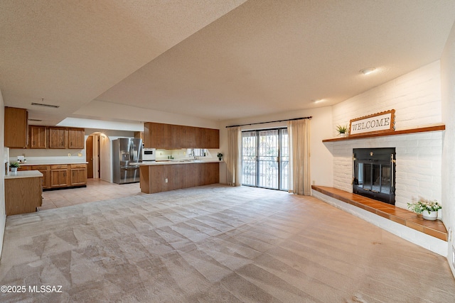 unfurnished living room featuring a textured ceiling, light colored carpet, and a brick fireplace