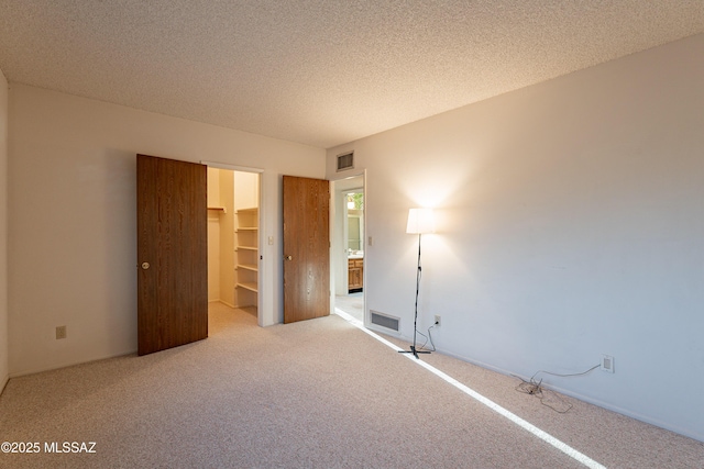 unfurnished bedroom with a textured ceiling, light colored carpet, a spacious closet, and a closet