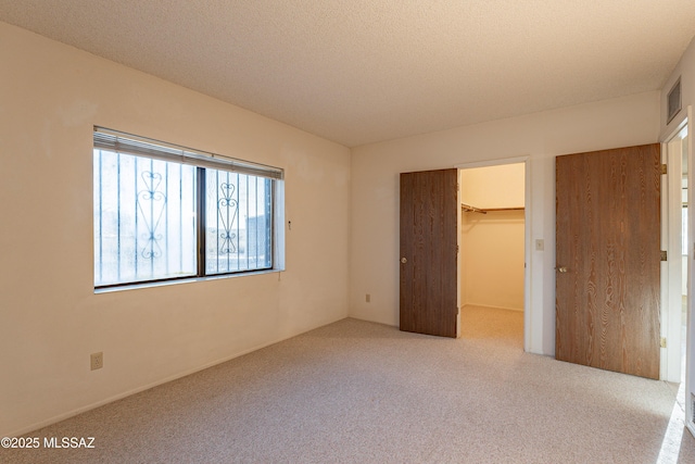 unfurnished bedroom with light colored carpet, a walk in closet, a textured ceiling, and a closet