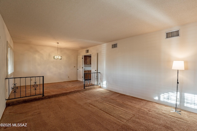 carpeted spare room featuring a textured ceiling and a chandelier