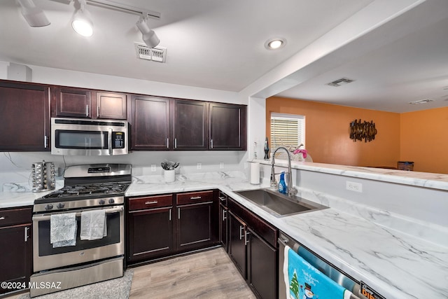 kitchen with appliances with stainless steel finishes, rail lighting, dark brown cabinetry, sink, and light hardwood / wood-style flooring