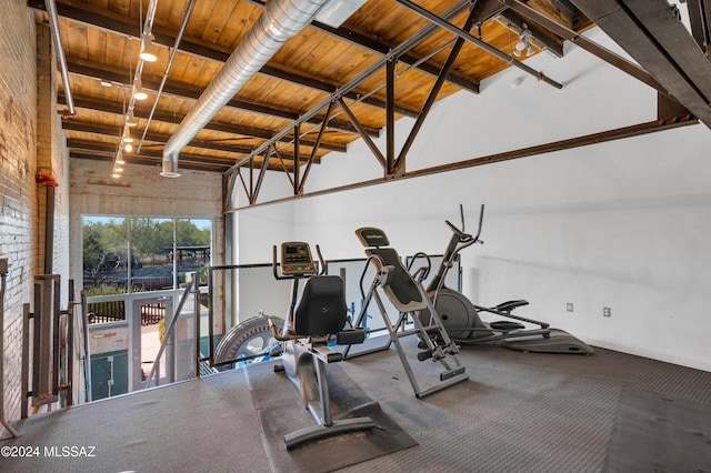 exercise area with wooden ceiling, rail lighting, a high ceiling, and brick wall