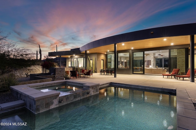 pool at dusk featuring an in ground hot tub and a patio