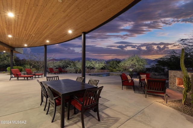 patio terrace at dusk with a mountain view and an outdoor stone fireplace