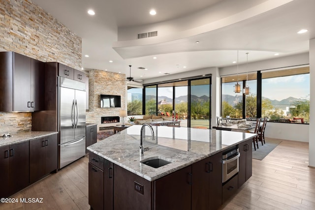 kitchen with sink, ceiling fan, a fireplace, an island with sink, and stainless steel appliances