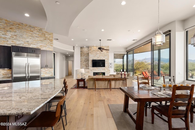 dining space with a fireplace, light wood-type flooring, and ceiling fan