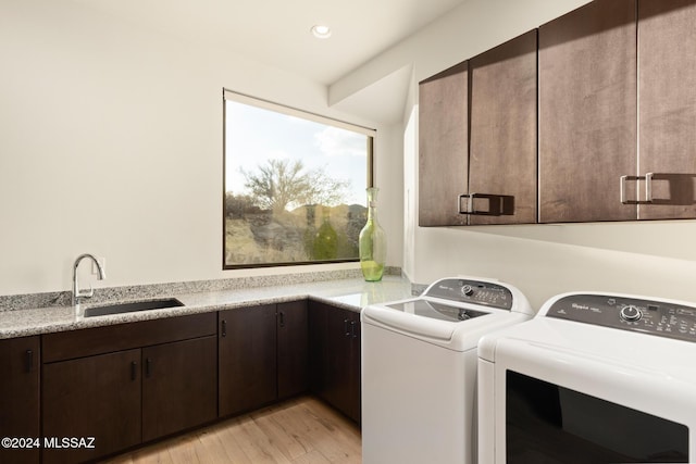 washroom featuring washing machine and clothes dryer, light hardwood / wood-style floors, cabinets, and sink