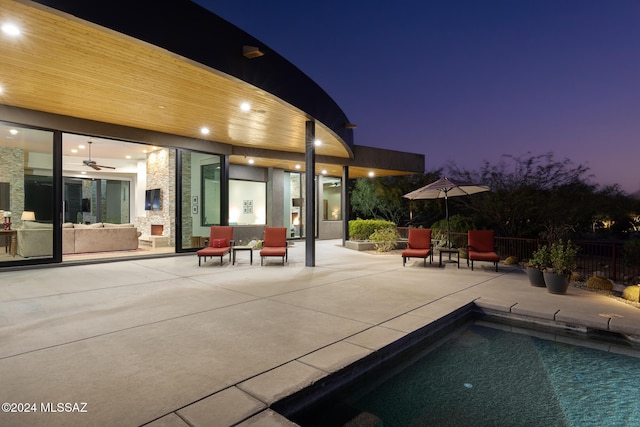 pool at dusk featuring ceiling fan and a patio