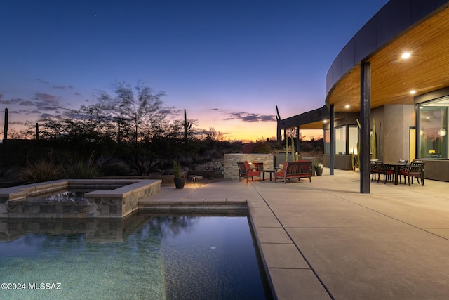 pool at dusk with an in ground hot tub and a patio