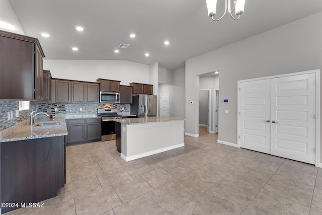 kitchen featuring light stone countertops, lofted ceiling, a kitchen island, stainless steel appliances, and sink