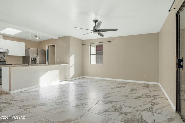 unfurnished living room featuring a skylight, ceiling fan, and beamed ceiling