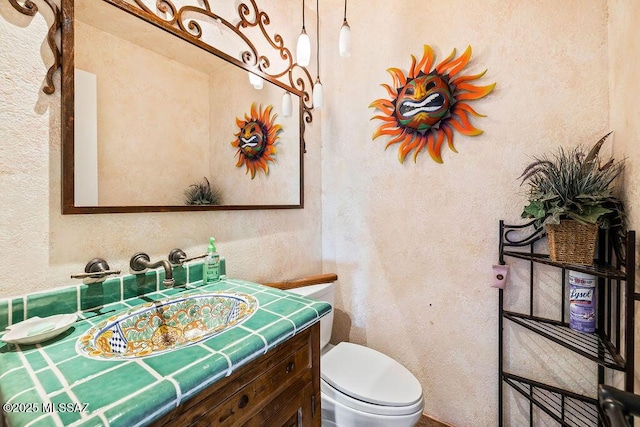 bathroom with a textured wall, vanity, and toilet