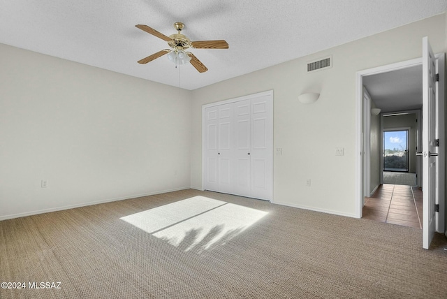 unfurnished bedroom with carpet flooring, ceiling fan, a textured ceiling, and a closet