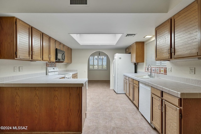 kitchen featuring white appliances, a chandelier, a raised ceiling, sink, and kitchen peninsula