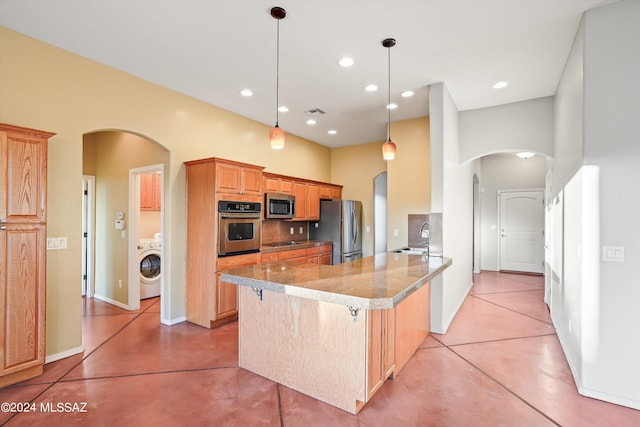 kitchen with sink, kitchen peninsula, washer / dryer, a breakfast bar, and appliances with stainless steel finishes