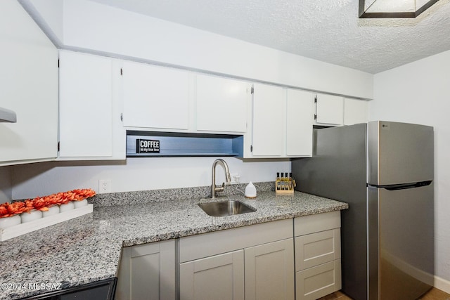 kitchen featuring stainless steel refrigerator, white cabinetry, sink, light stone counters, and a textured ceiling