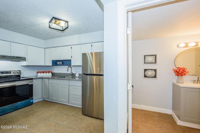 kitchen with appliances with stainless steel finishes, a textured ceiling, under cabinet range hood, a sink, and light tile patterned flooring