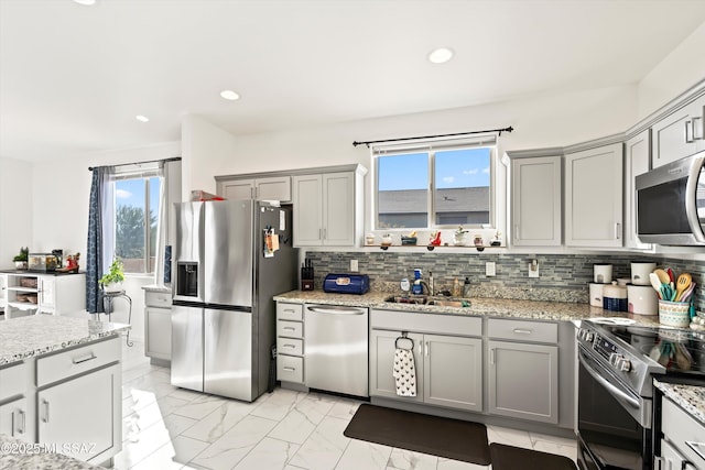 kitchen with appliances with stainless steel finishes, light stone countertops, and sink