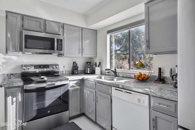 kitchen with gray cabinetry, a sink, light stone counters, stainless steel appliances, and light tile patterned floors