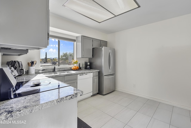 kitchen featuring dishwasher, gray cabinets, range, freestanding refrigerator, and a sink