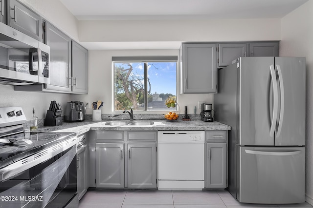 kitchen with light stone counters, gray cabinets, stainless steel appliances, and a sink