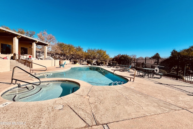 pool with a patio, a community hot tub, and fence