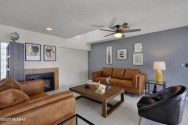 living room with ceiling fan, a brick fireplace, light tile patterned floors, and a textured ceiling