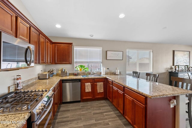 kitchen with sink, dark hardwood / wood-style floors, kitchen peninsula, a breakfast bar area, and stainless steel appliances