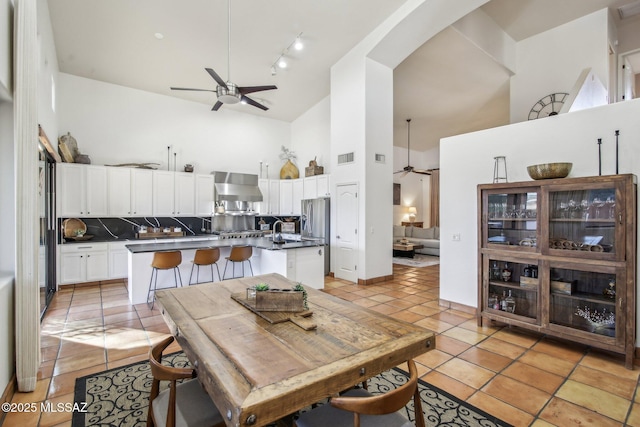 tiled dining space with ceiling fan, sink, and high vaulted ceiling