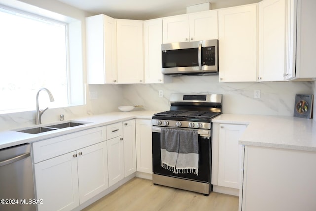 kitchen with white cabinetry, sink, stainless steel appliances, tasteful backsplash, and light hardwood / wood-style flooring