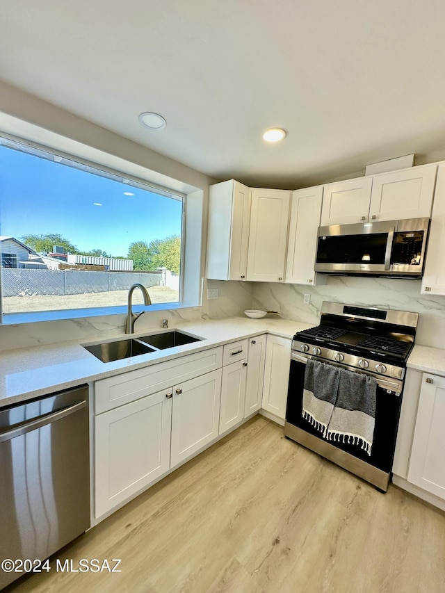 kitchen with tasteful backsplash, stainless steel appliances, sink, light hardwood / wood-style flooring, and white cabinets